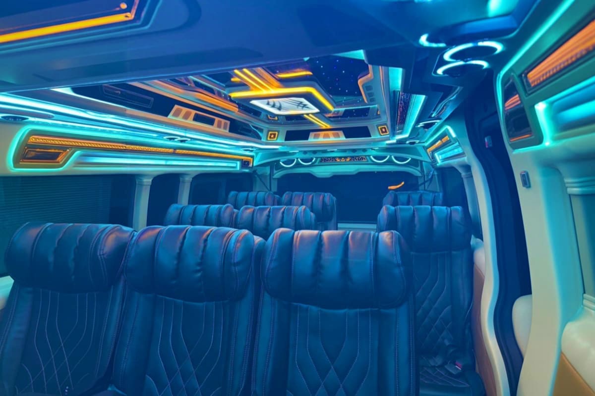 Luxury coach bus interior with blue leather seats and neon cyan and gold ceiling lighting