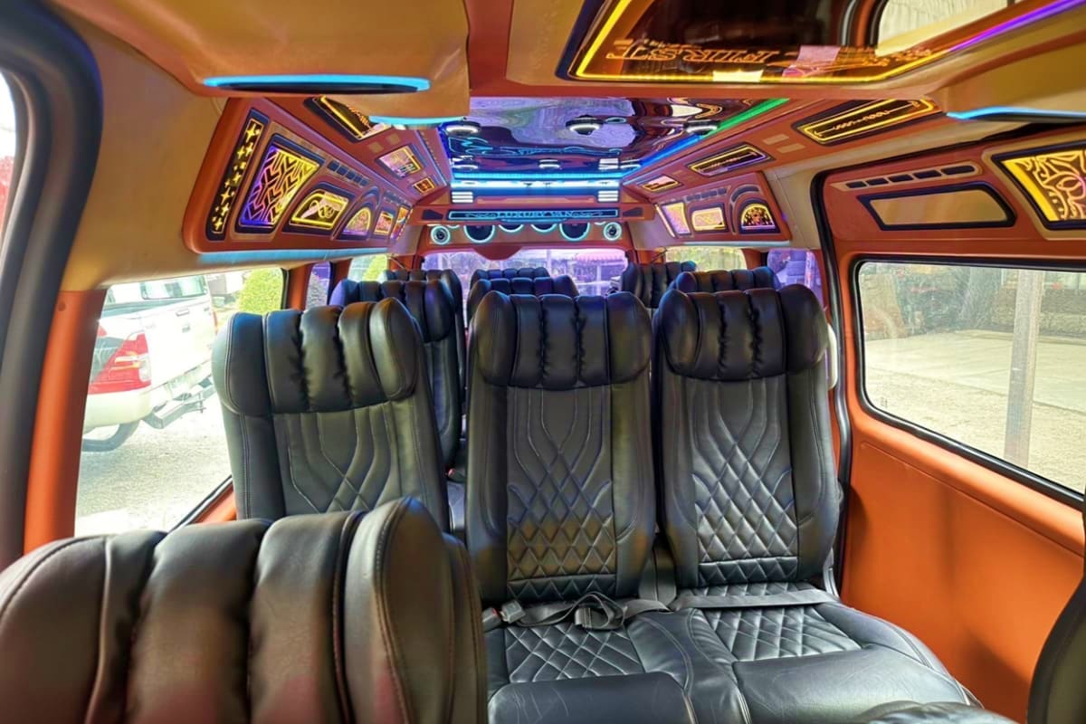 Luxury tour bus interior with black quilted seats, colorful LED ceiling lights, and decorative wood paneling