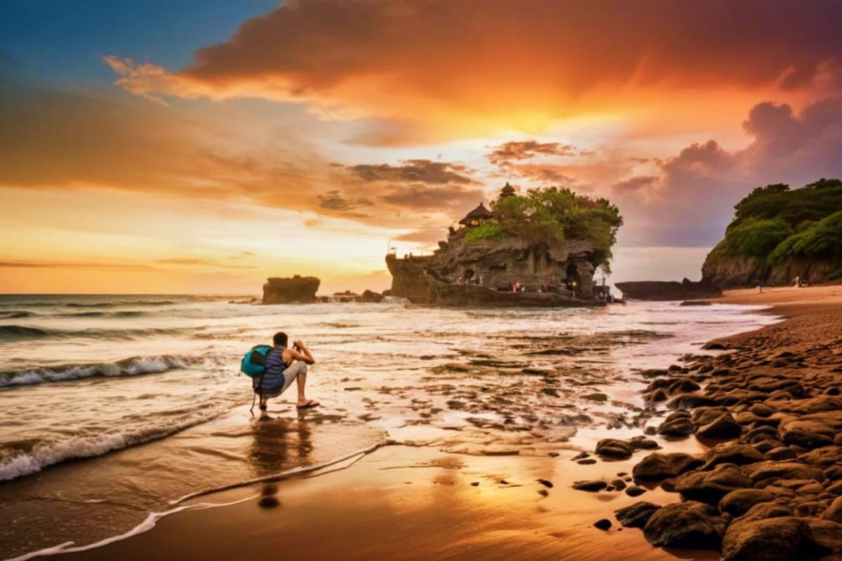 Photographer shooting Tanah Lot temple at sunset with golden sky and ocean waves on Bali beach