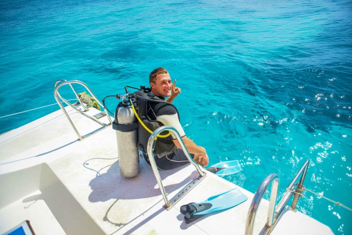 Tanjung Benoa Water Sports Diver in full scuba gear sitting on boat deck with air tank and fins, prepared for diving in clear turquoise ocean water
