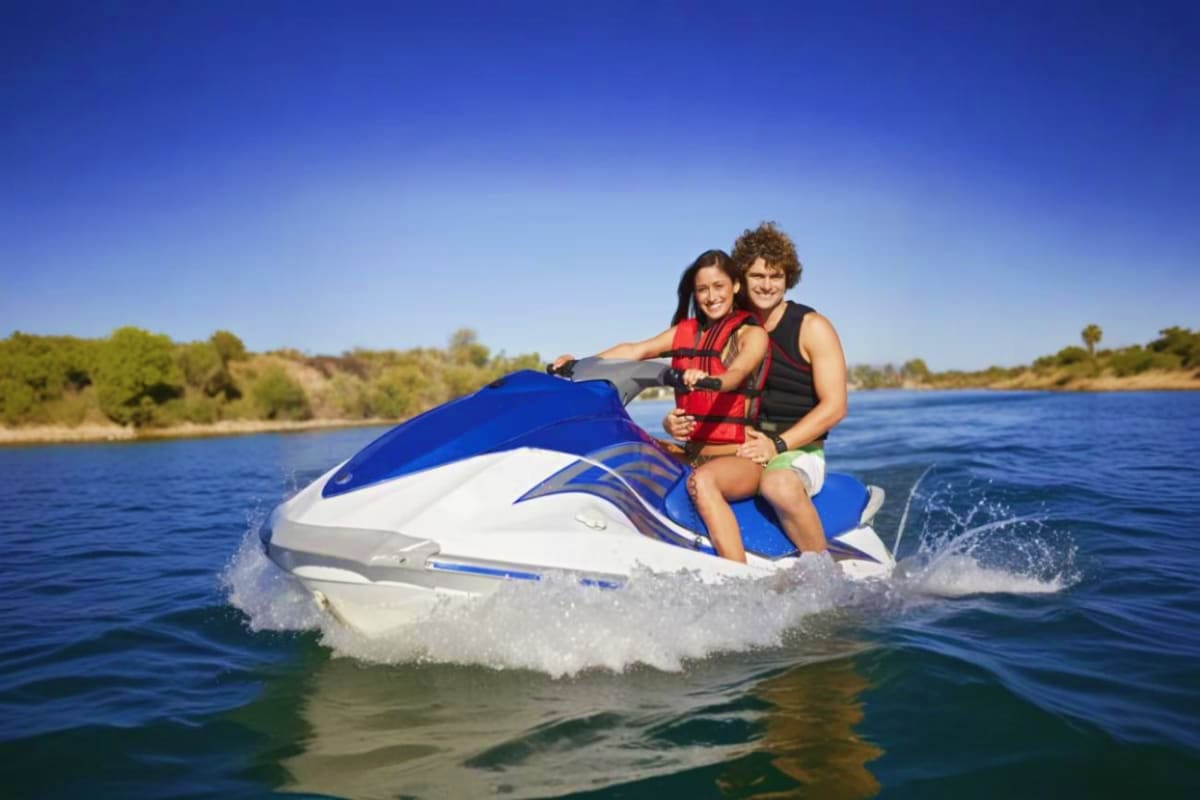 Tanjung Benoa Water Sports Couple riding a blue and white jet ski on calm water with green shoreline and trees in background at Tanjung Benoa