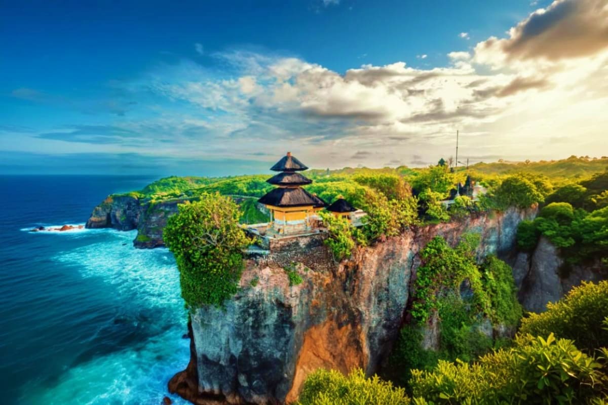 Uluwatu Temple perched on a cliff overlooking turquoise ocean waters with lush green vegetation in Bali, Indonesia
