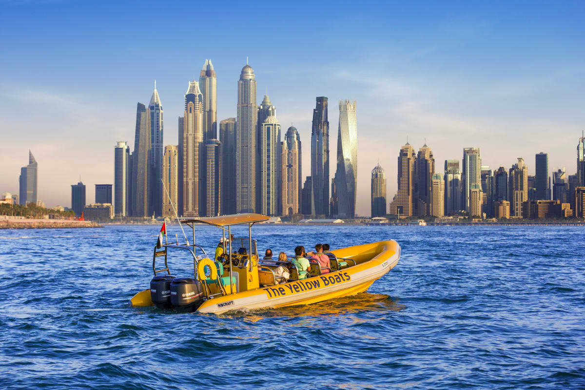 Yellow speedboat tour with passengers on Dubai waters with city skyline and tall buildings in background