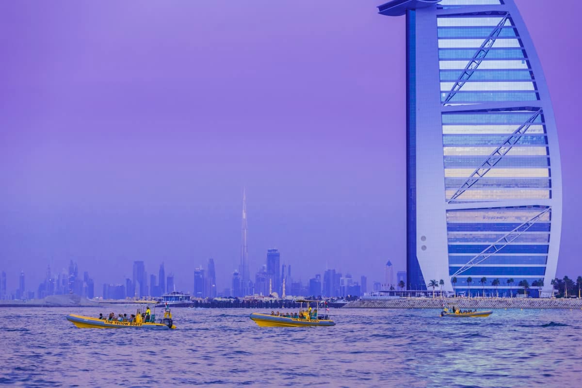 Yellow boats in Dubai waters with Burj Al Arab hotel and city skyline in background at sunset