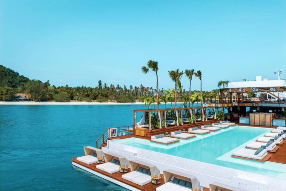 Yona Beach Club with turquoise pool, white loungers, and palm trees overlooking clear blue ocean water and sandy beach