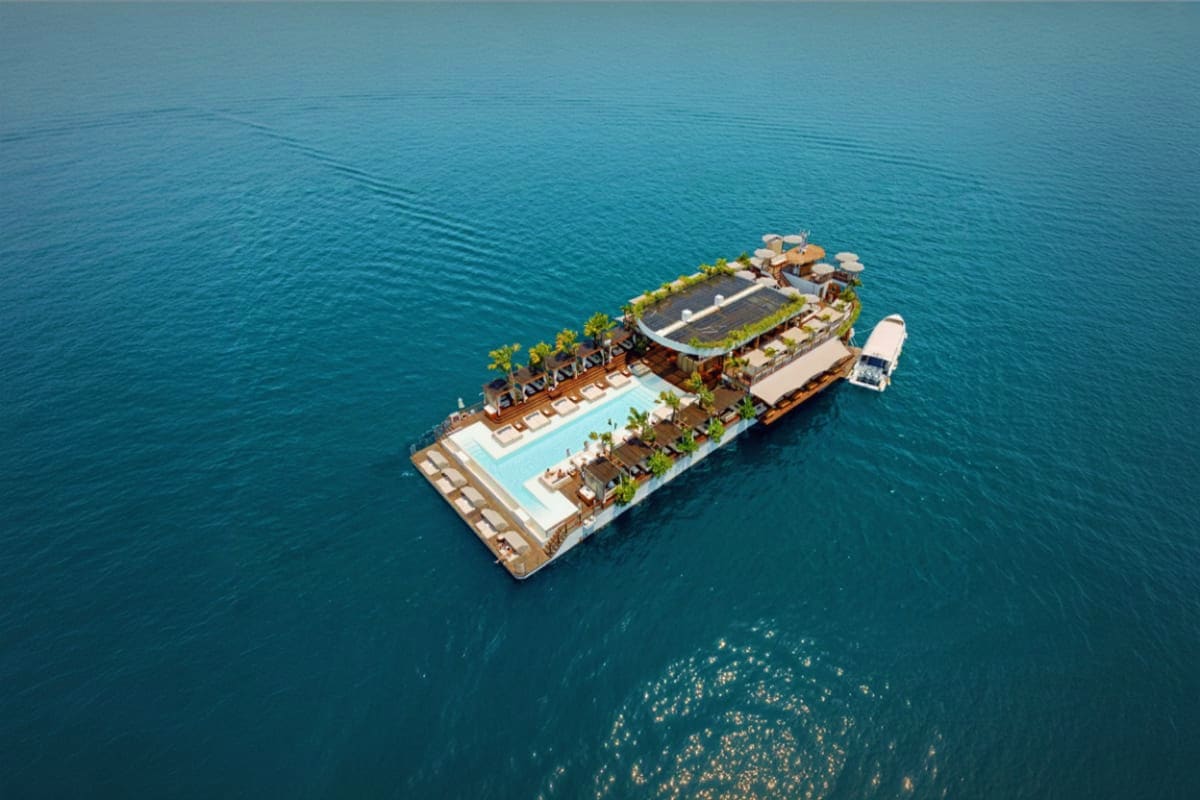 Aerial view of Yona Beach Club floating platform with swimming pool, lounge chairs, and covered dining area on turquoise sea 
