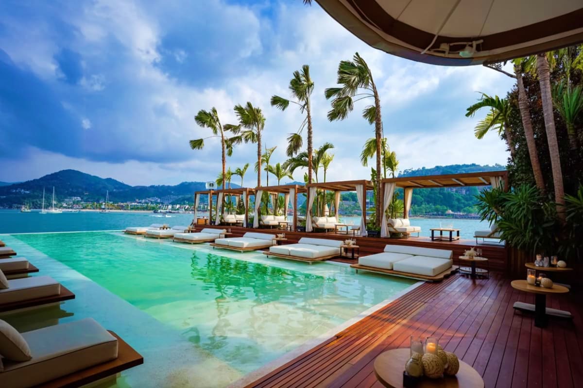 Yona Beach Club luxury poolside lounge with turquoise water, palm trees, wooden deck, and mountain views across bay