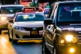 Multiple taxis with headlights on lined up in traffic during daytime intercity transfer service