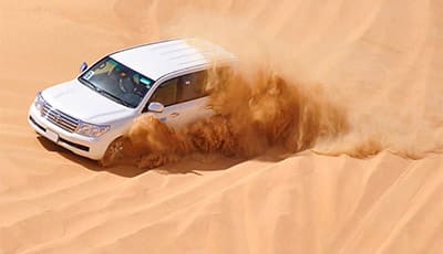 White SUV driving through sandy desert dunes creating dust cloud during dune bashing activity in Jeddah