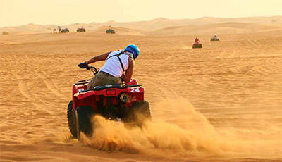 Jeddah Safari with Quad Bikes and Camel Ride Person riding red quad bike through sandy desert creating dust cloud with other vehicles visible in background