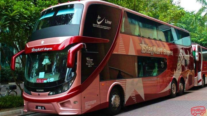 Red double-decker StarMart Express coach bus parked on street surrounded by tropical vegetation