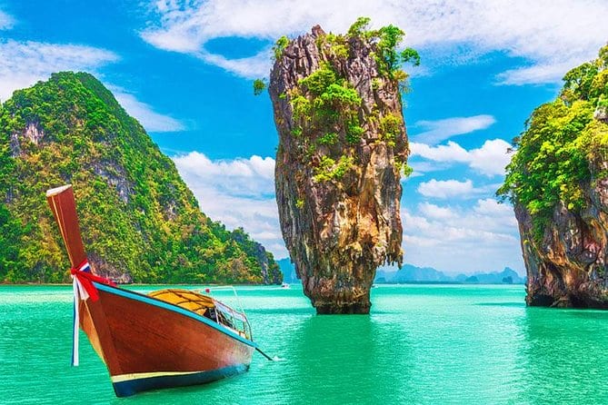Traditional red and yellow long tail boat near limestone rock formations in turquoise water at James Bond Island, Thailand