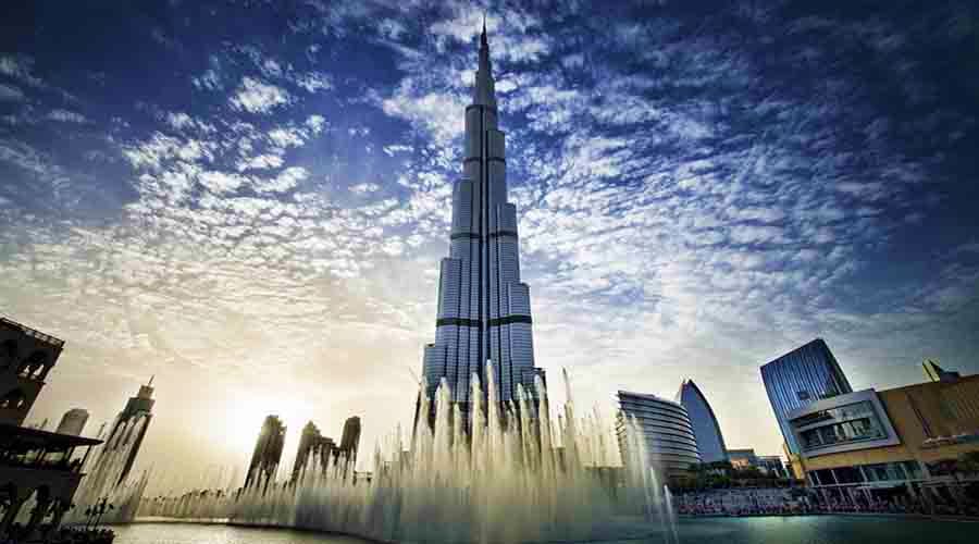 Dubai Fountain Show Lake ride from Ras Al Khaimah Burj Khalifa tower with illuminated fountain jets spraying water in Dubai lake against cloudy blue sky