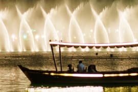 Dubai Fountain Show Lake ride from Ras Al Khaimah Traditional wooden boat on water with Dubai Fountain illuminated jets in background at night
