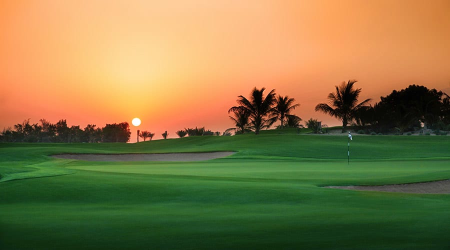 Golf course at sunset with manicured fairways, sand bunkers, palm trees, and flag marker at Emirates Golf Club