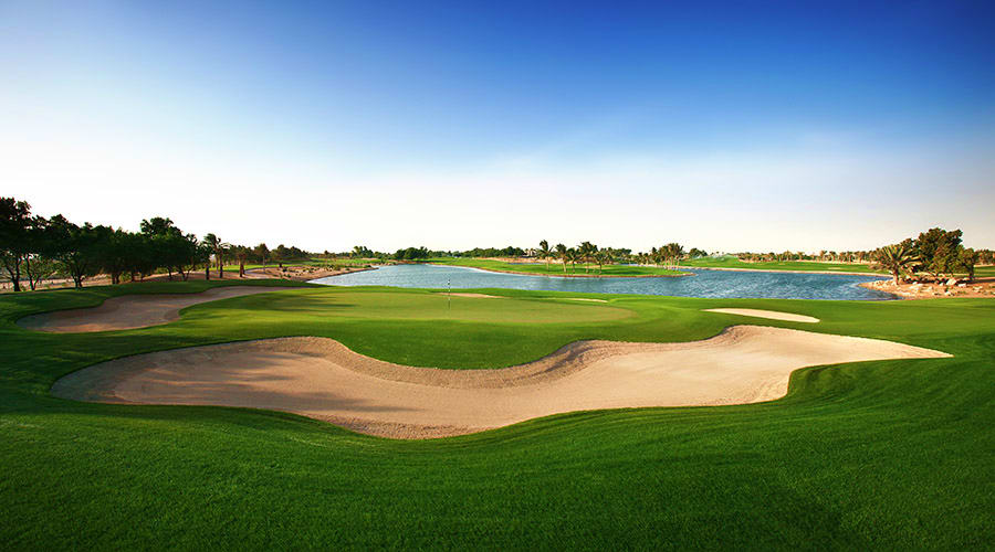 Professional golf course with manicured green fairway, sand bunker, and water hazard under clear blue sky at Emirates Golf Cl