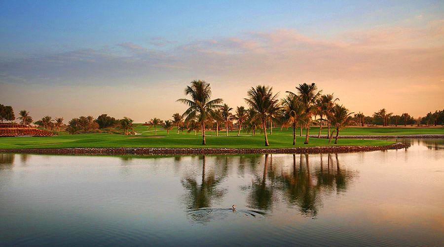 Serene golf course at Emirates Golf Club with manicured green fairway, palm trees, and calm water reflection at sunset