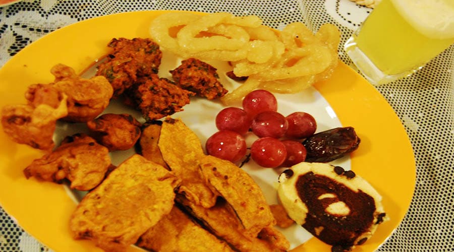 Yellow plate with fried appetizers, onion rings, red grapes, and baked goods on lace tablecloth, Iftar meal setup