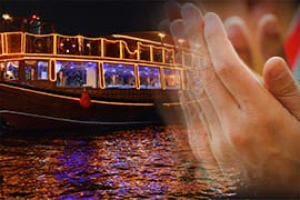 Hand in foreground with traditional wooden abra boat on Dubai Creek at night during Iftar celebration with lights