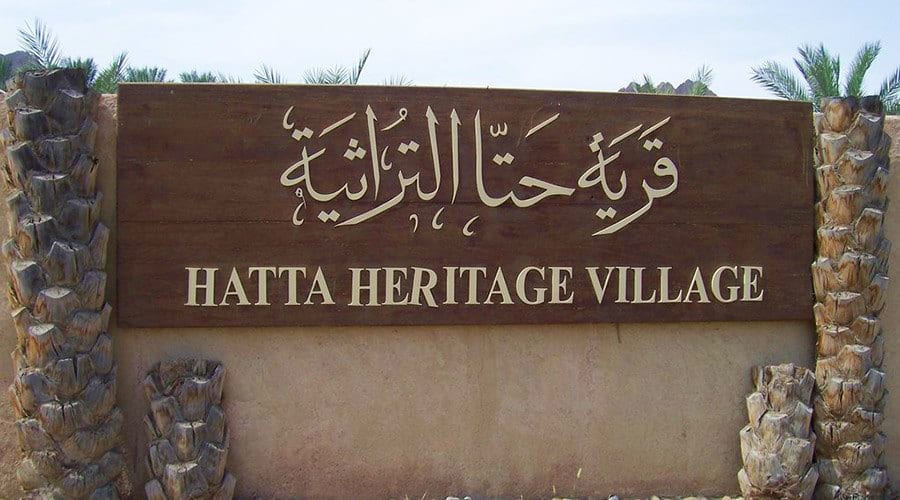 Hatta Heritage Village entrance sign with Arabic and English text flanked by decorative palm tree pillars