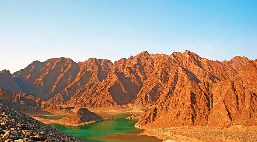 Turquoise mountain lake surrounded by dramatic rocky peaks and arid desert landscape in Hatta