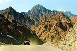 Jeep driving on dusty mountain road through rocky desert terrain in Hatta Mountains