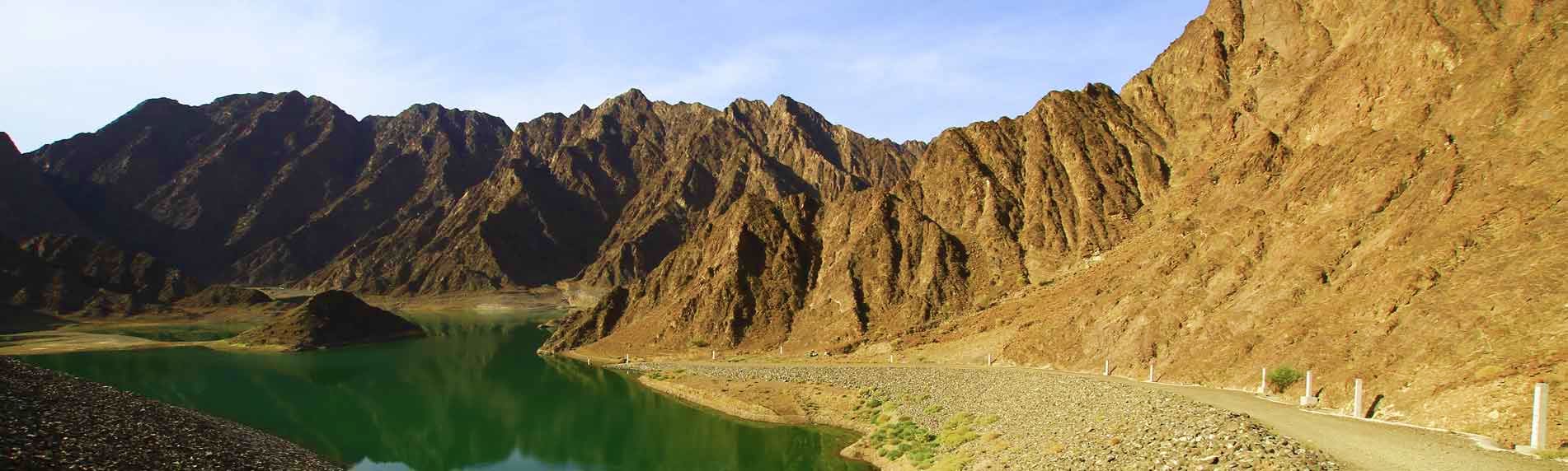 Hatta Mountain Safari Rugged desert mountains with turquoise lake and gravel road in Hatta mountain landscape, United Arab Emirates