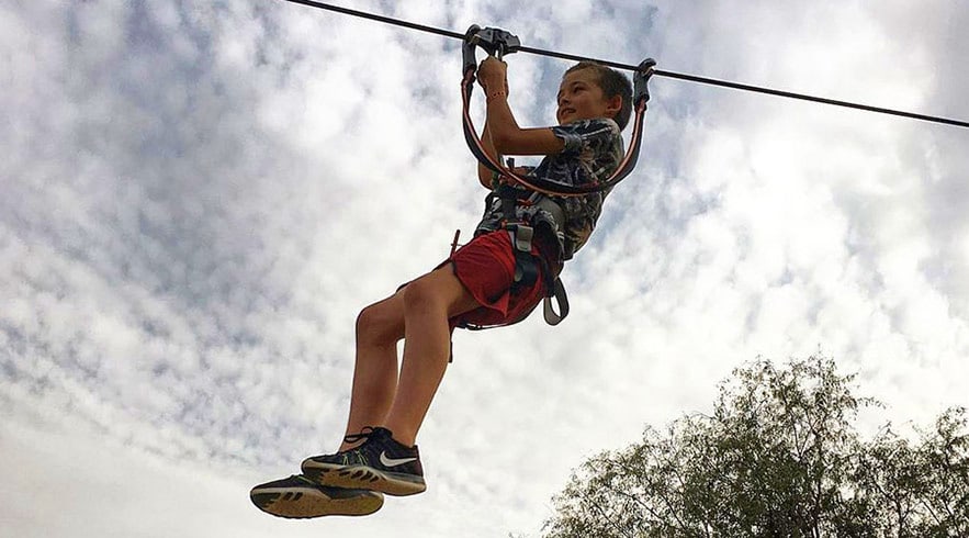 Aventura Parks Dubai Person ziplining on cable course at Aventura Parks Dubai with cloudy sky and trees below