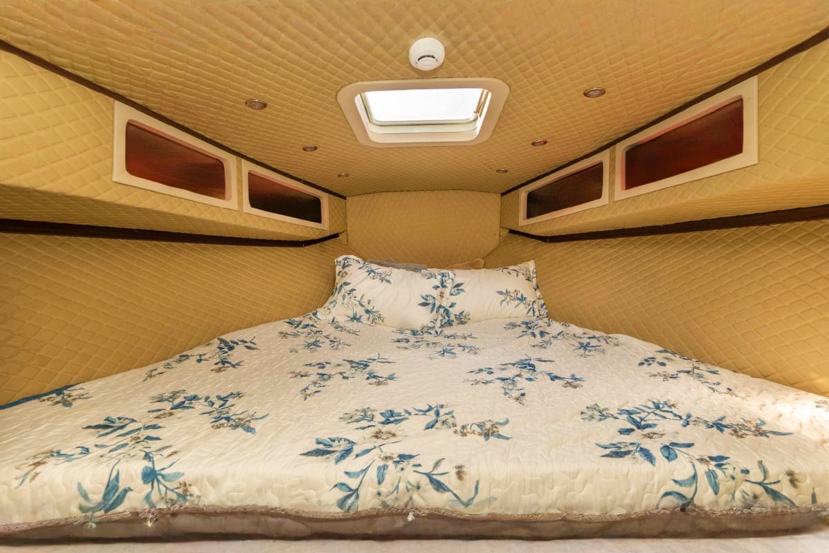 Interior view of RV bedroom with queen bed, floral bedding, wood paneling, overhead skylight, and storage cabinets
