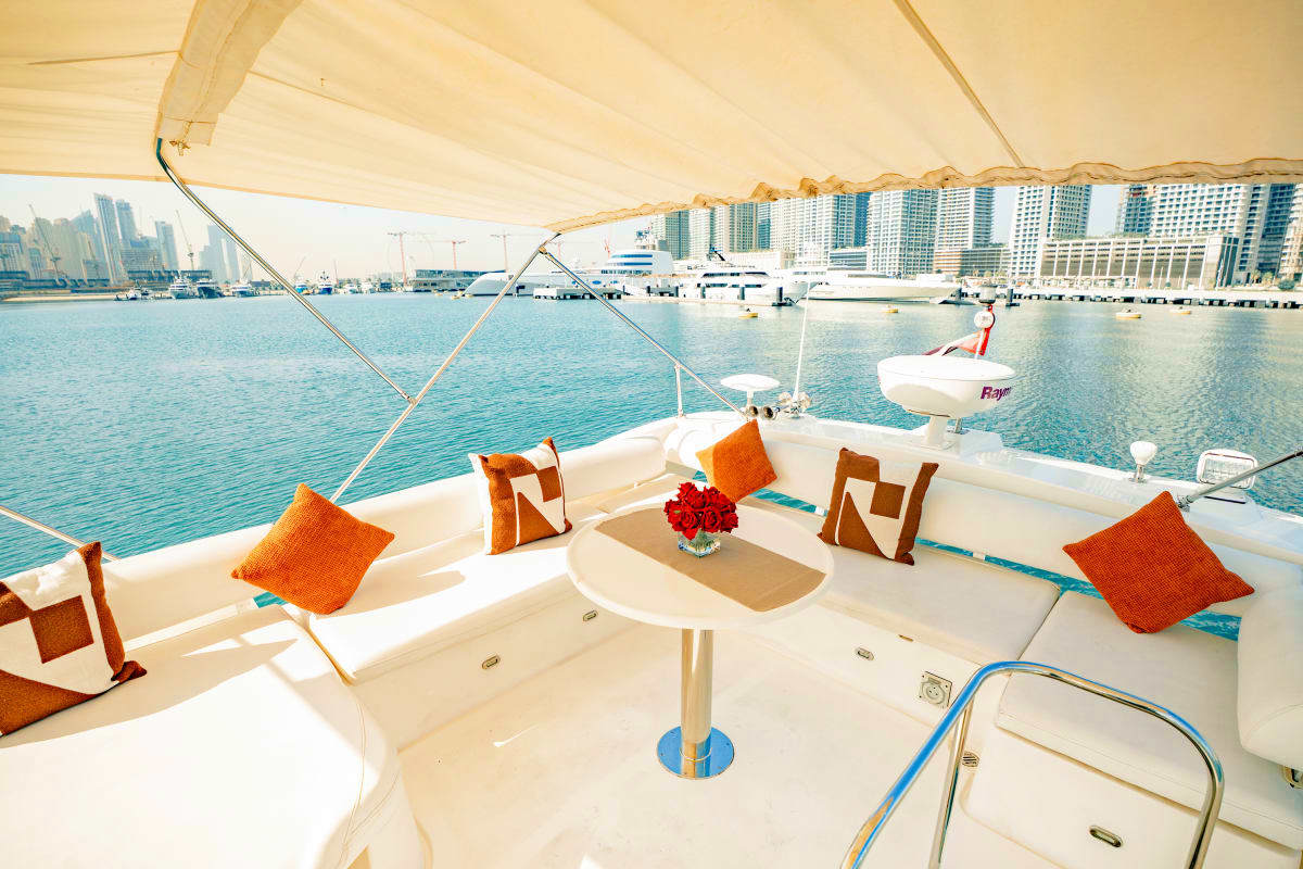 Luxury yacht deck with cream canvas canopy, orange cushions, and central table overlooking marina with high-rise buildings an