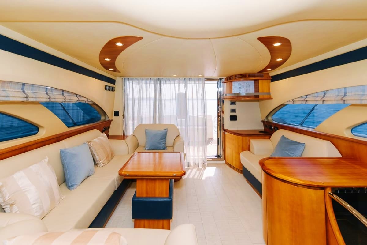 Luxury yacht interior cabin with cream seating, wood furnishings, porthole windows with ocean views, and modern curved ceilin