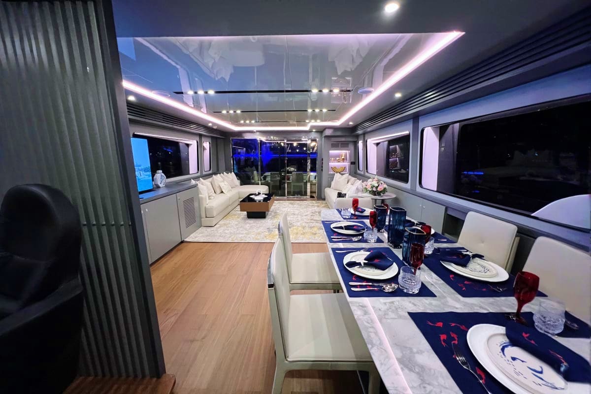 Luxury yacht interior with formal dining area, white seating, ambient ceiling lighting, and panoramic night ocean views throu