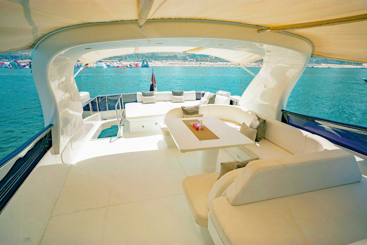 Maiora X12 Maiora X12 luxury yacht flybridge with white seating, dining table, and turquoise Mediterranean coastline view