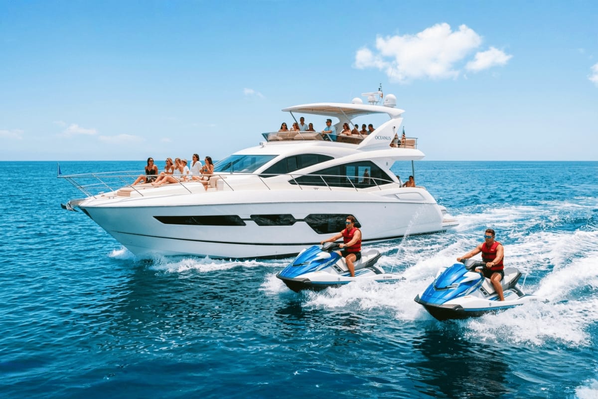 Luxury white yacht with passengers on upper deck and sun pad, two people riding blue jet skis in turquoise ocean water with w