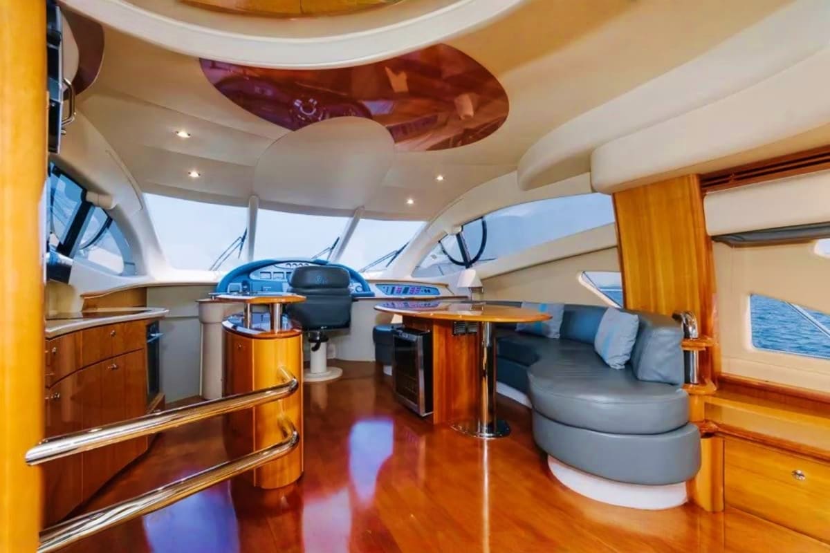 Luxurious yacht interior cabin with wooden finishes, steering wheel, gray seating, and panoramic windows overlooking the ocea