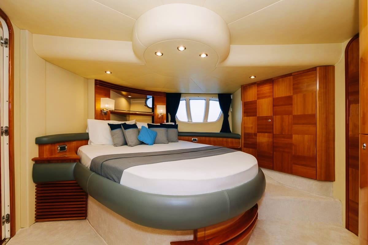 Luxury yacht master bedroom with round bed, wood cabinetry, cream walls, porthole window, and recessed lighting