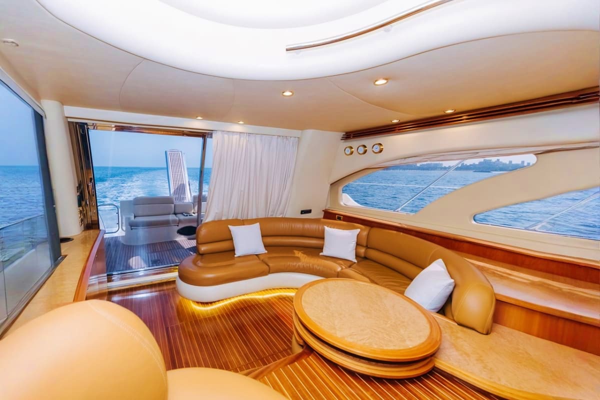Luxury yacht interior with tan leather curved seating, round wooden table, and ocean views through large windows
