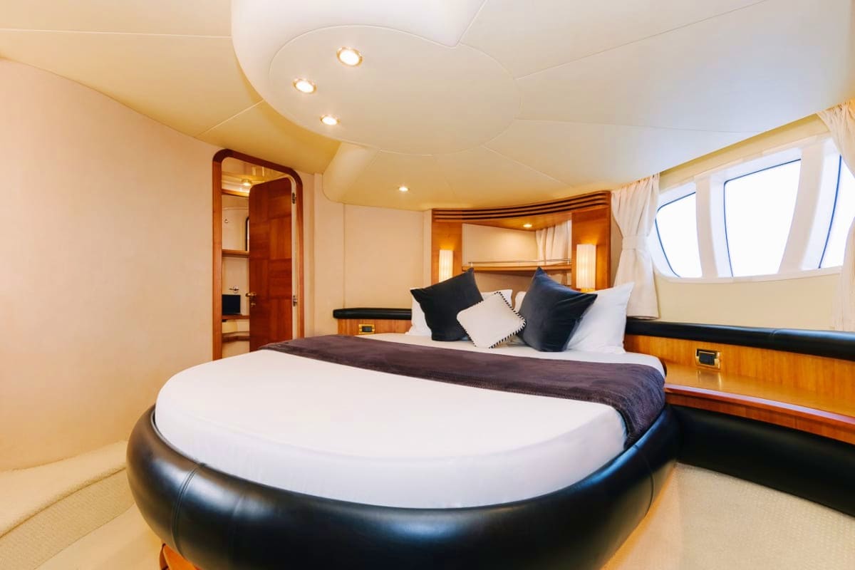 Luxury yacht master bedroom with round bed, black and white pillows, wooden cabinetry, porthole windows, and recessed lightin