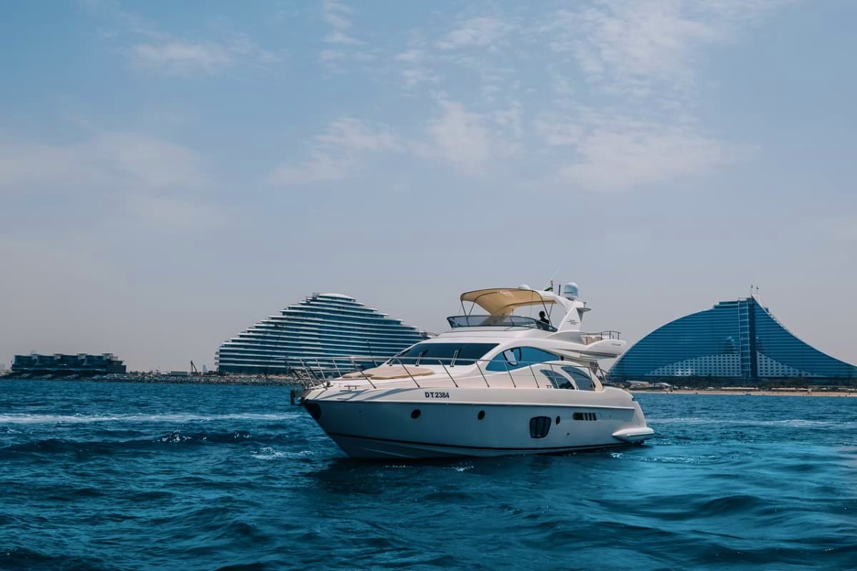 White luxury yacht anchored in turquoise water with modern architecture buildings in background under clear sky