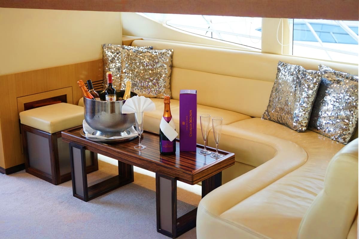 Luxury yacht cabin interior with cream leather seating, wood table with champagne bucket, glasses, and purple bottle, silver 