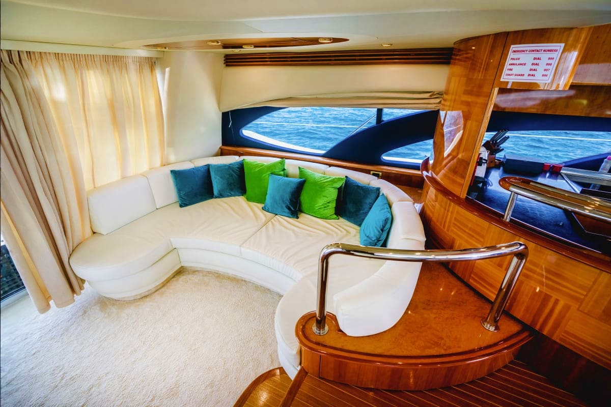 Luxurious yacht cabin interior with white curved seating, blue and green cushions, wooden paneling, and ocean views through l