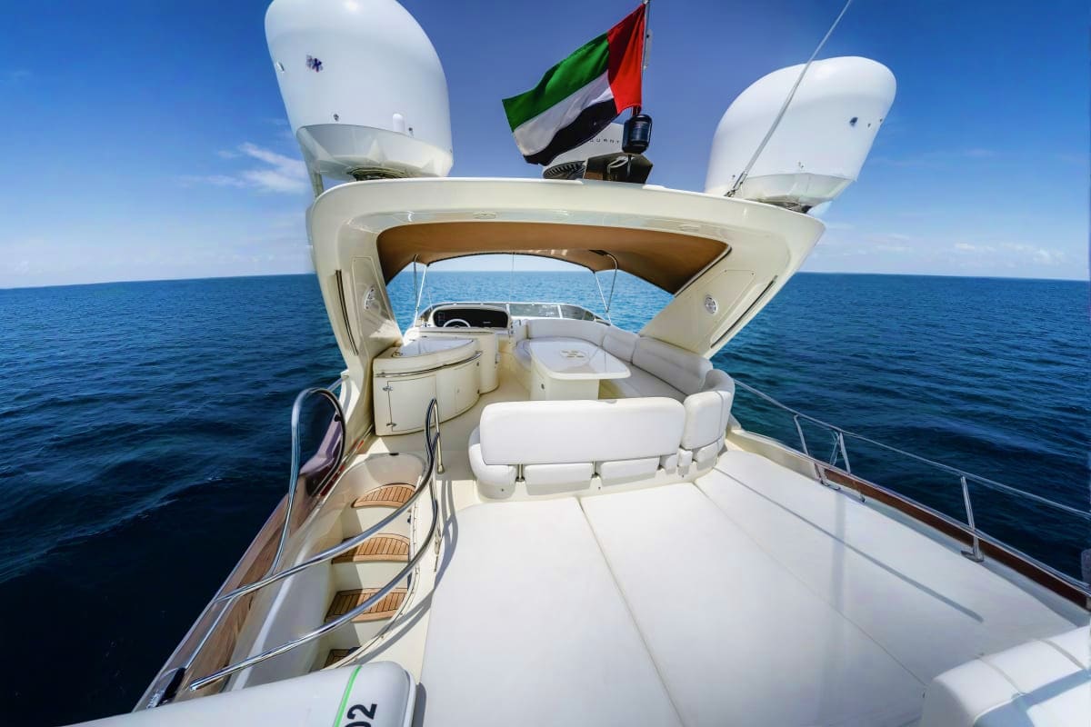 Luxury white yacht deck with UAE flag, white seating area, satellite antennas, and calm blue ocean on clear day