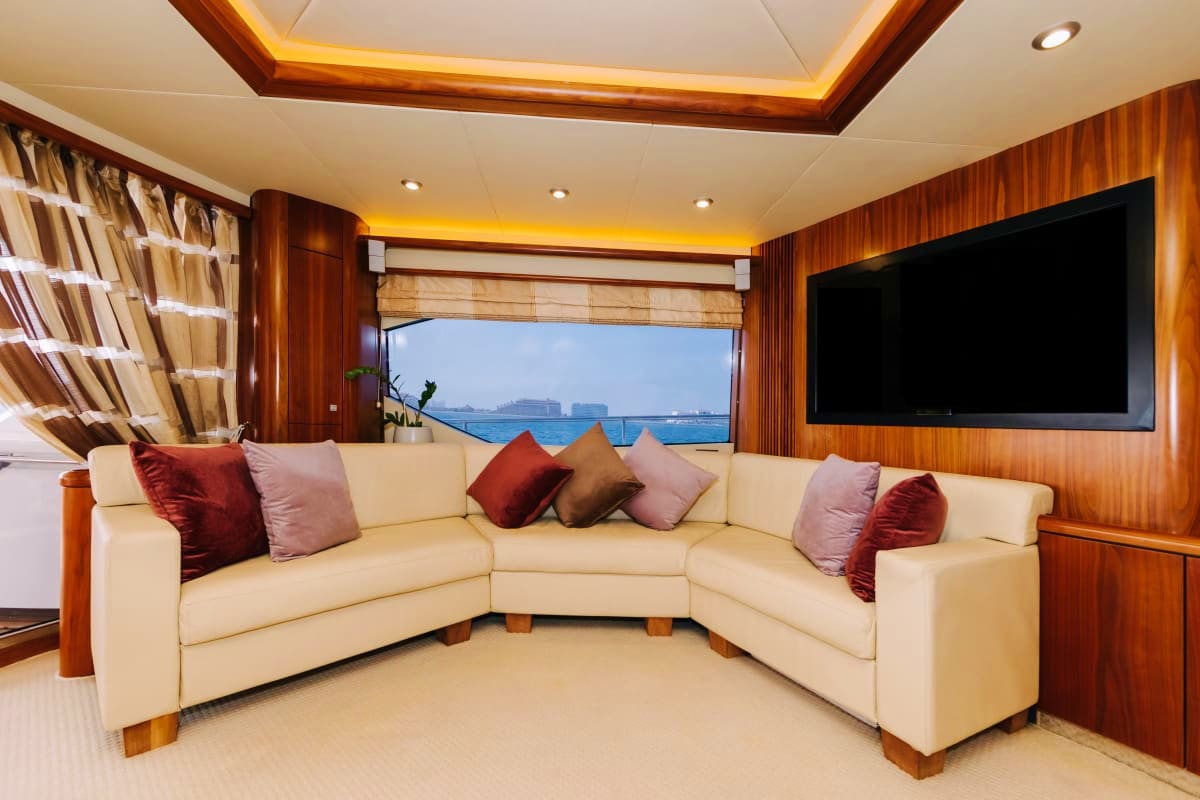 Luxury yacht interior salon with cream sectional sofa, wood paneling, flat-screen TV, and ocean views through large windows
