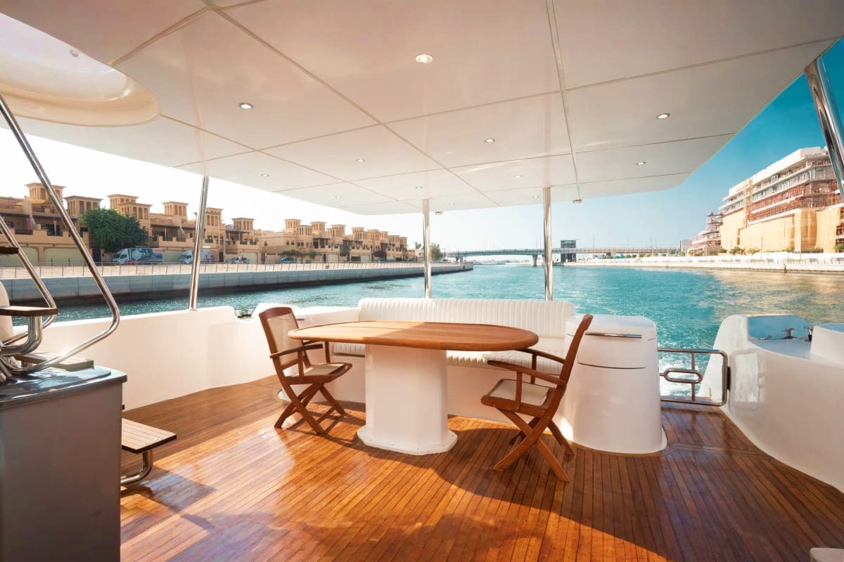 85 Ft KRONOS Yacht upper deck with wooden table, chairs, and white retractable canopy overlooking Dubai Marina waterfront