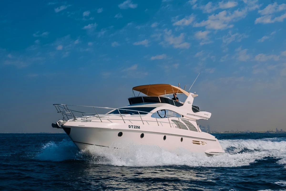 White luxury motor yacht with tan canopy anchored in ocean waves under blue sky