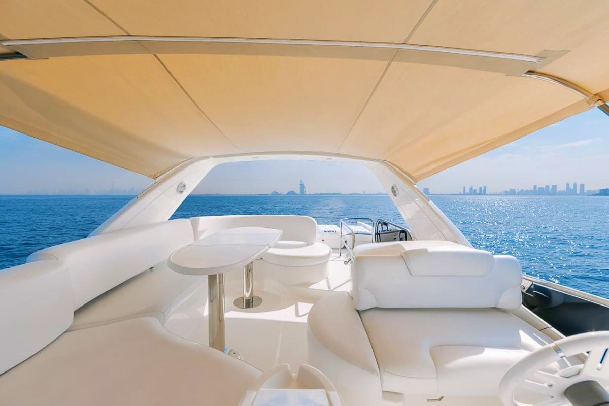 Luxury white yacht cabin with beige canopy, seating area, and steering wheel overlooking blue ocean with city skyline in dist
