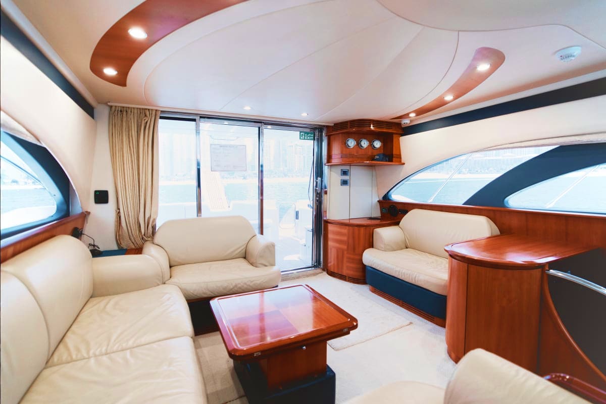 Luxury yacht interior cabin with cream leather seating, wooden furnishings, curved white ceiling, and ocean views through lar
