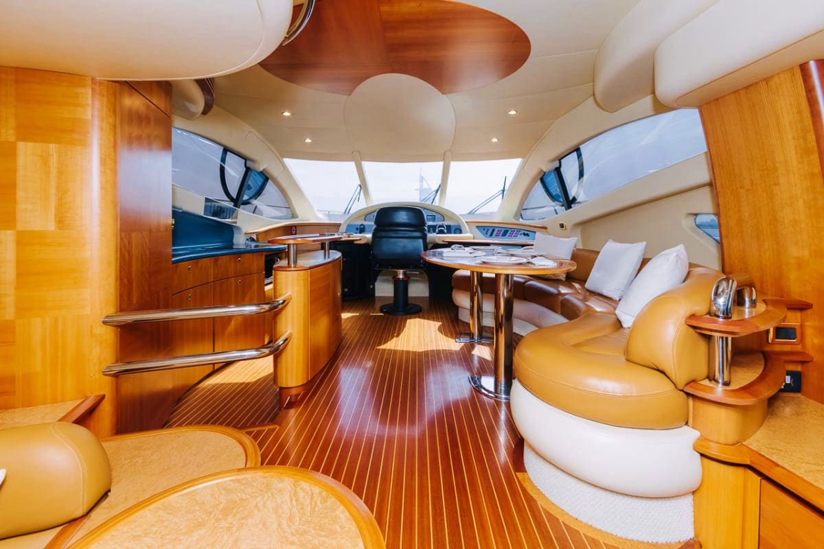 Luxury yacht interior with wooden cabinetry, cream seating, steering wheel, and teak flooring with natural sunlight from over