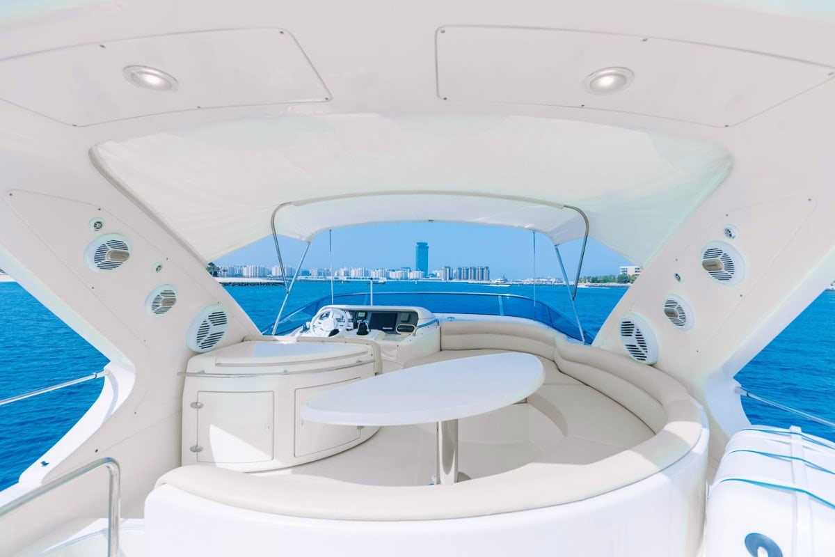 Interior view of 55 Ft My Choice Yacht cabin with white seating, circular table, and blue water and coastal cityscape visible