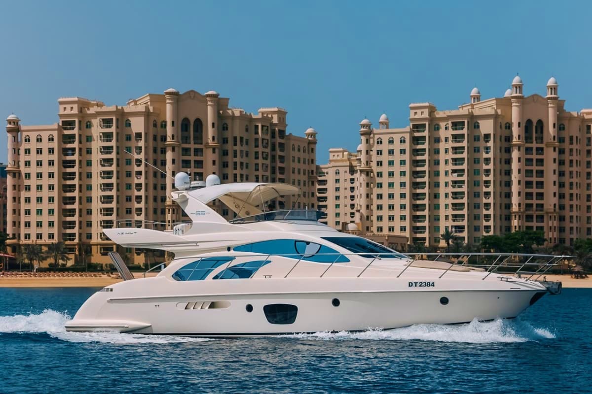 Luxury white and blue 55-foot motor yacht cruising in turquoise waters with beige high-rise residential buildings in backgrou